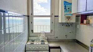 A compact kitchen with a gas stove, oven, and a window with a view of the sea. - Charming Mar del Plata Apartment With Ocean Views (Mar del Plata)