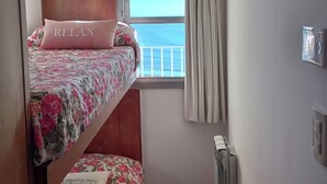 A small, cozy room with a bunk bed, a window with a view of the sea, and a radiator. - Charming Mar del Plata Apartment With Ocean Views (Mar del Plata)