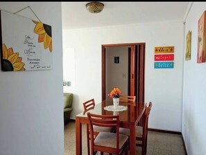 A dining area with a wooden table and chairs, a vase with flowers, and a wall with a welcome sign and a 'Happy Birthday' sign. - Charming Mar del Plata Apartment With Ocean Views (Mar del Plata)