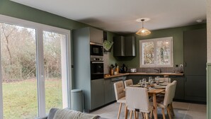 A modern kitchen with a dining area, large windows, and a view of the outdoors. - Gîte "Gîte Du Pré Simon" with Private Garden and Wi-Fi (Le Faulq)