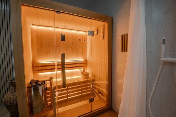 A sauna with wooden benches, a bench with a bowl, and a glass door.