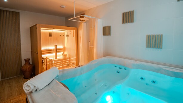 A modern spa room with a large hot tub, wooden door, and a small table with chairs. - Gîte "Gîte Du Pré Simon" with Private Garden and Wi-Fi (Le Faulq)