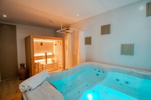 A modern spa room with a large hot tub, wooden door, and a small table with chairs.
