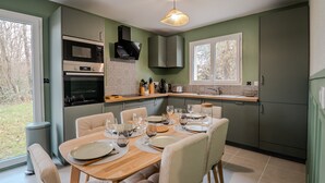 A modern kitchen with a dining area, equipped with appliances, a large window, and a view of the outdoors. - Gîte "Gîte Du Pré Simon" with Private Garden and Wi-Fi (Le Faulq)