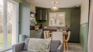 A modern kitchen with a dining area, a sofa, and a window with a view of trees. - Gîte "Gîte Du Pré Simon" with Private Garden and Wi-Fi (Le Faulq)