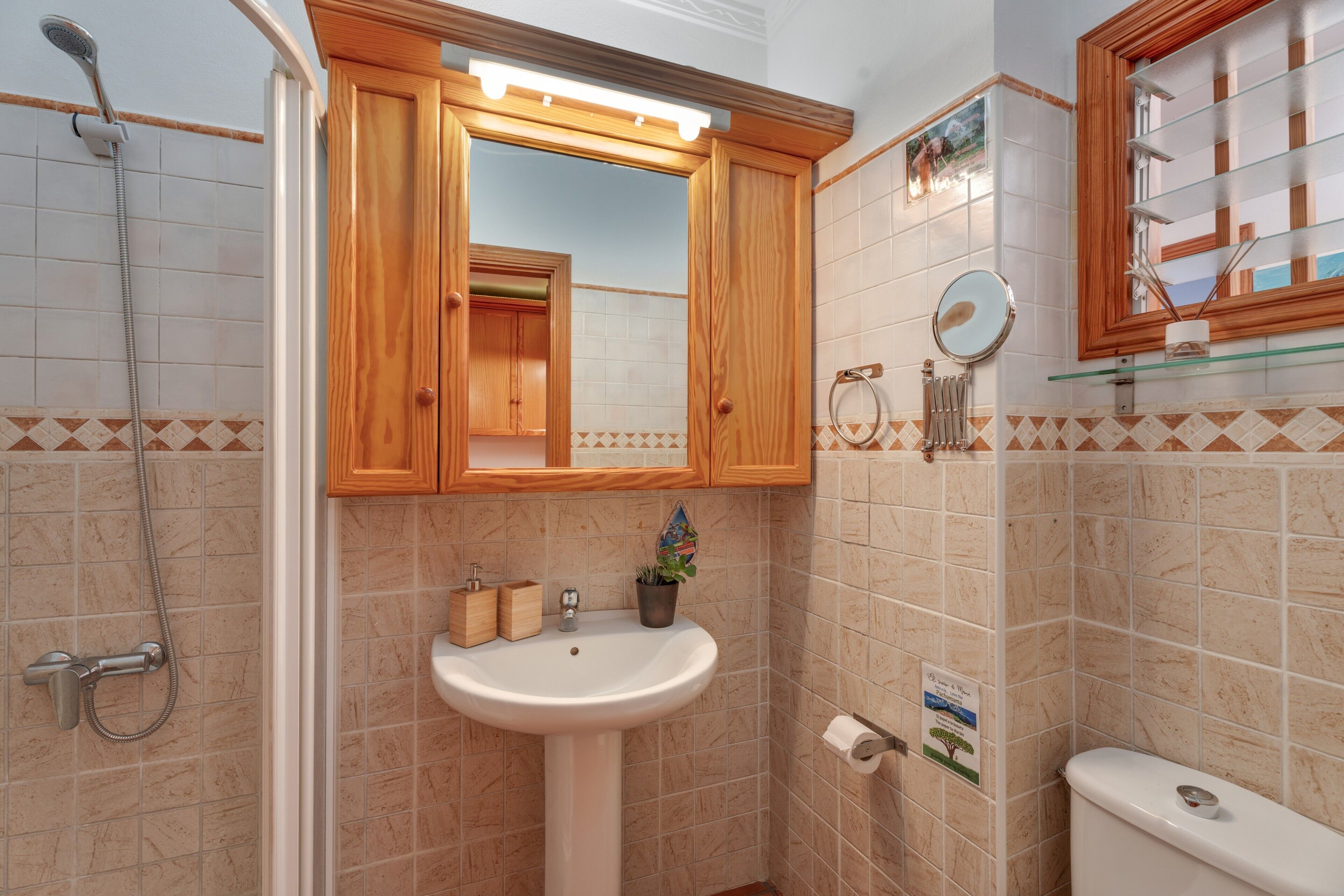 Un baño con tocador de madera, lavamanos, espejo, ducha e inodoro.