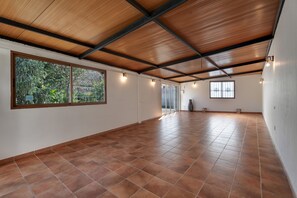 Una habitación amplia con suelo de baldosas, ventanas grandes y techo de madera.