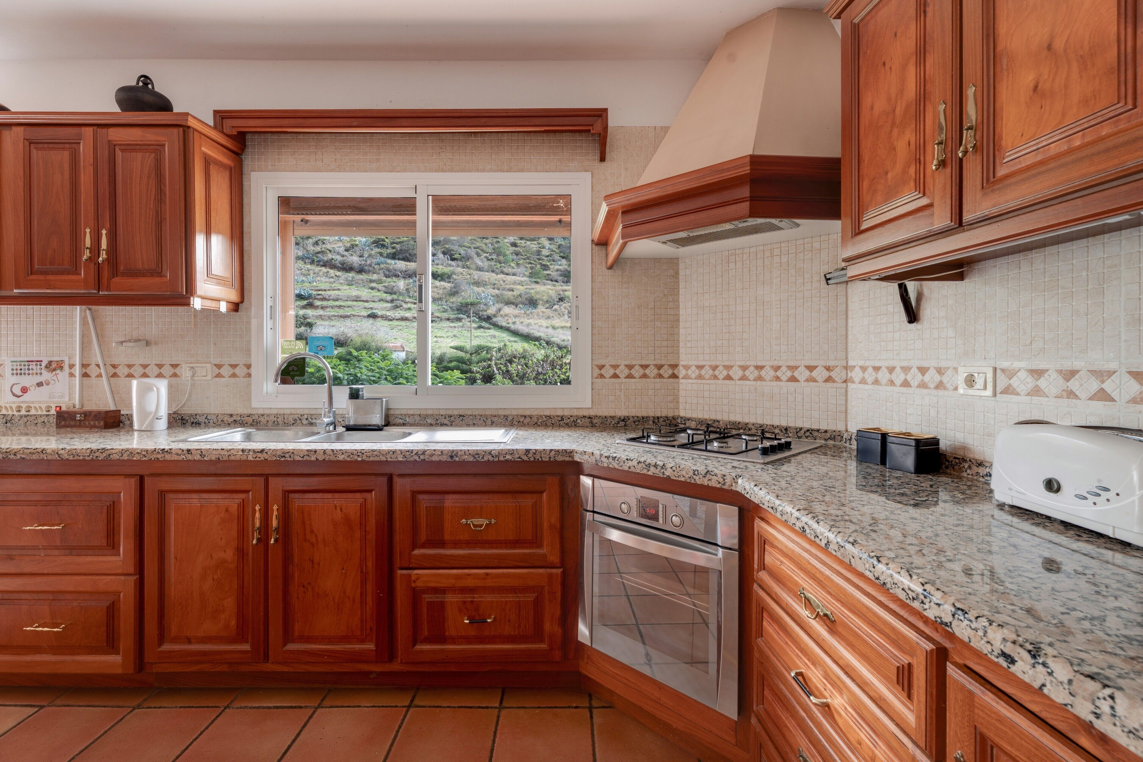 Una cocina con armarios de madera, encimera de granito, ventana con vistas y horno empotrado.