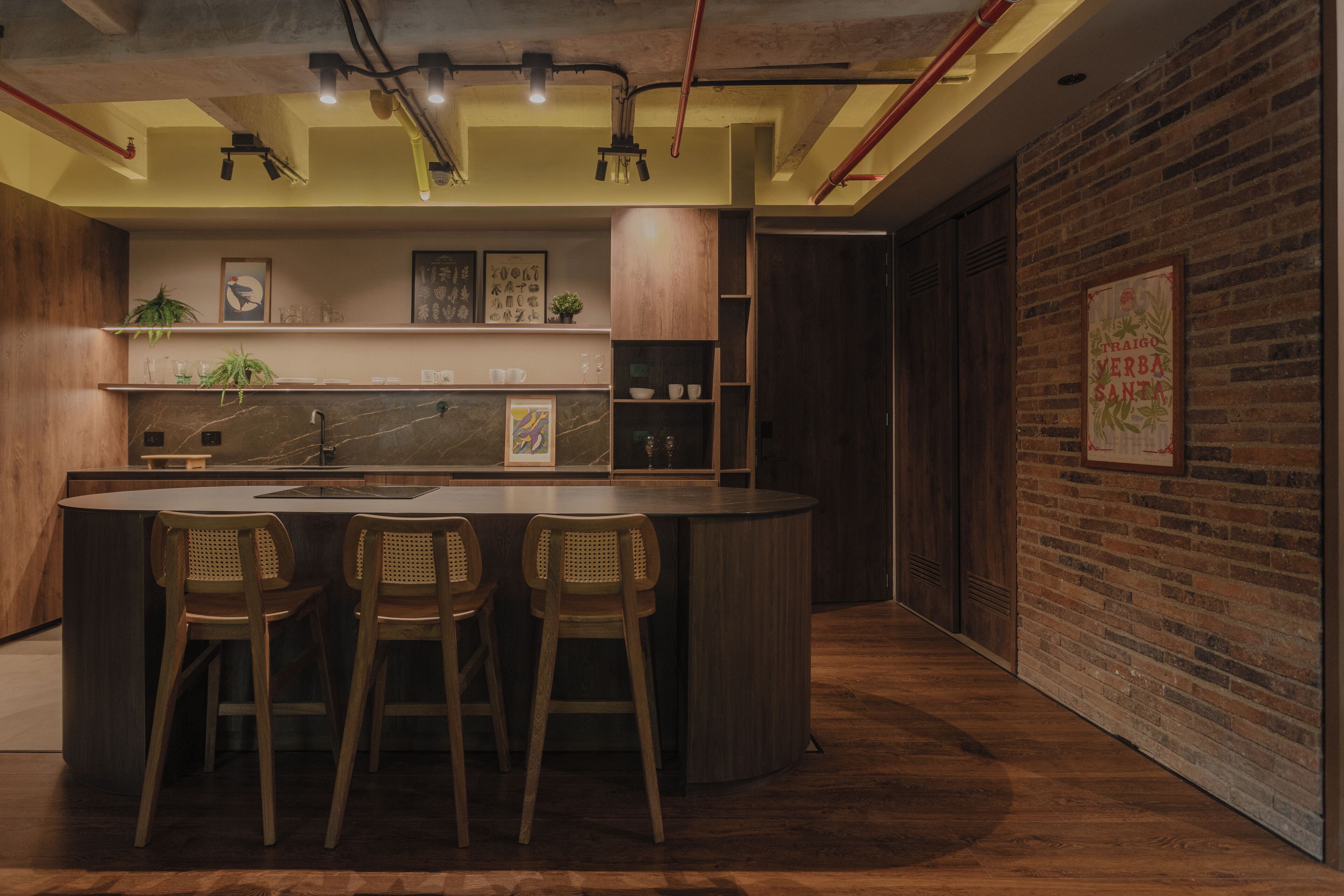 Una cocina moderna con una isla central, taburetes de bar, armarios de madera y una pared de ladrillo.