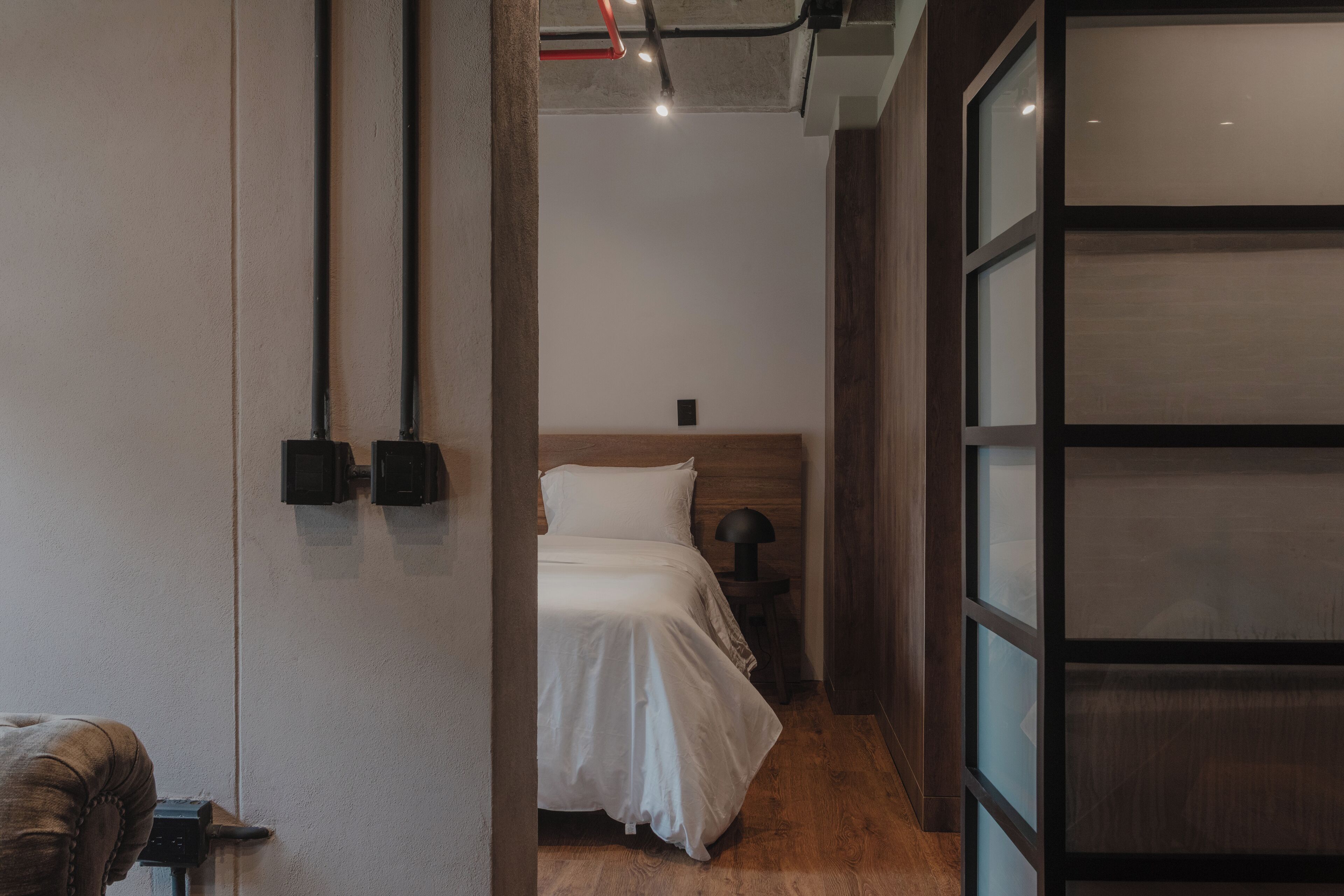 Quarto moderno com cabeceira de madeira, abajur e vista através de uma porta de vidro.