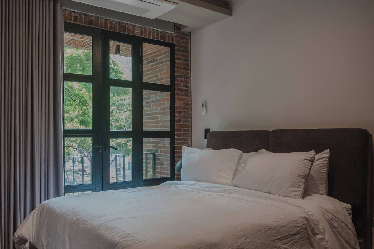 Una habitación de hotel moderna con una cama grande, vistas al exterior y un techo con vigas y luces a la vista.
