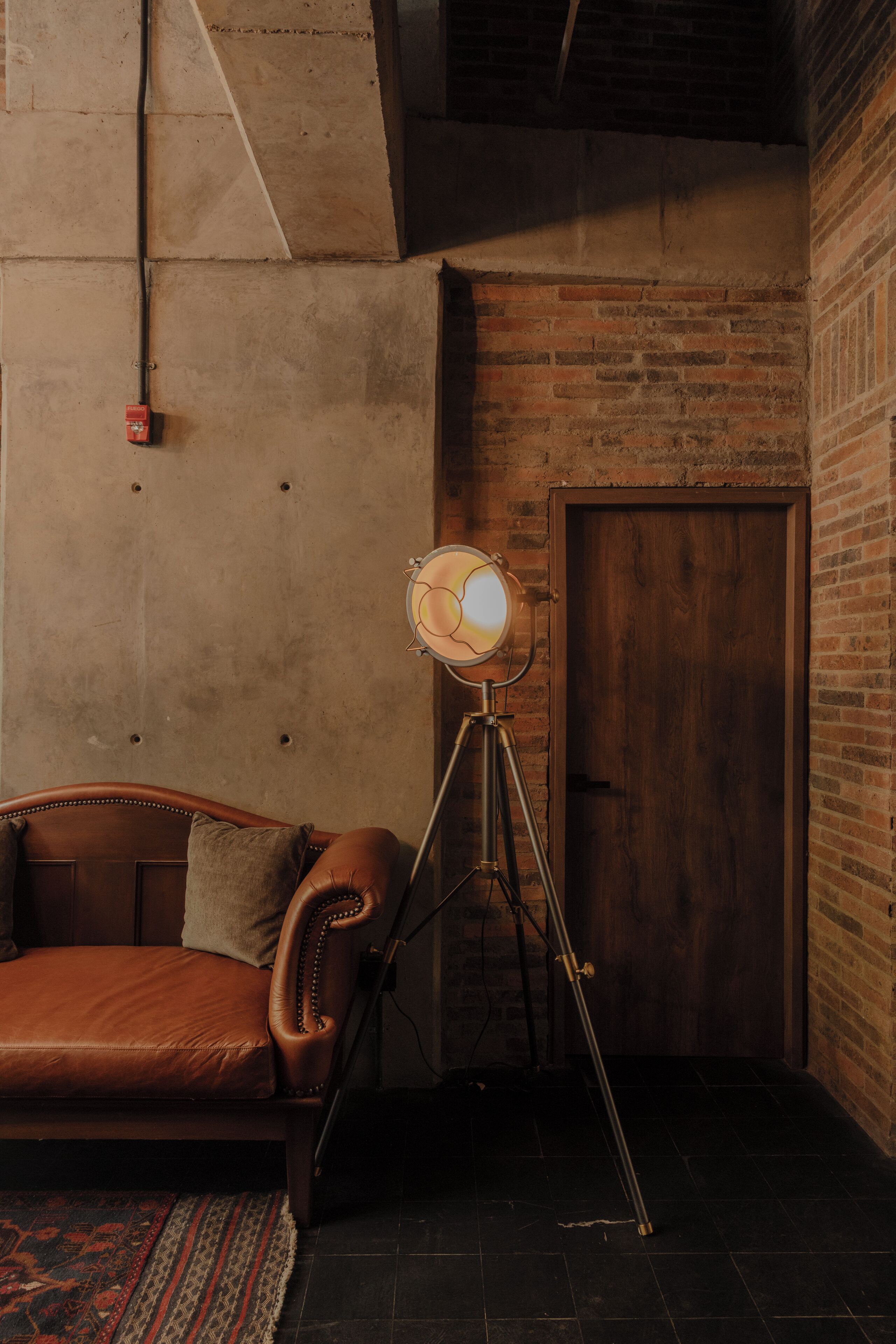 Une pièce avec un canapé en cuir, un lampadaire, une porte en bois et un mur en briques.
