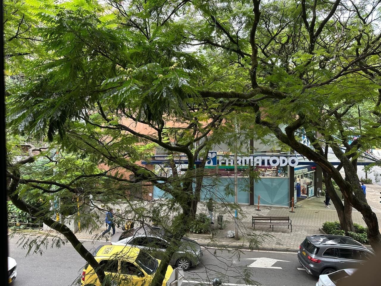 A street view with a pharmacy named 'Farmatodo' and a yellow taxi in the foreground.