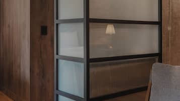 Una habitación con piso de madera, un sillón tapizado en gris y un separador alto y estrecho con paneles de vidrio esmerilado.