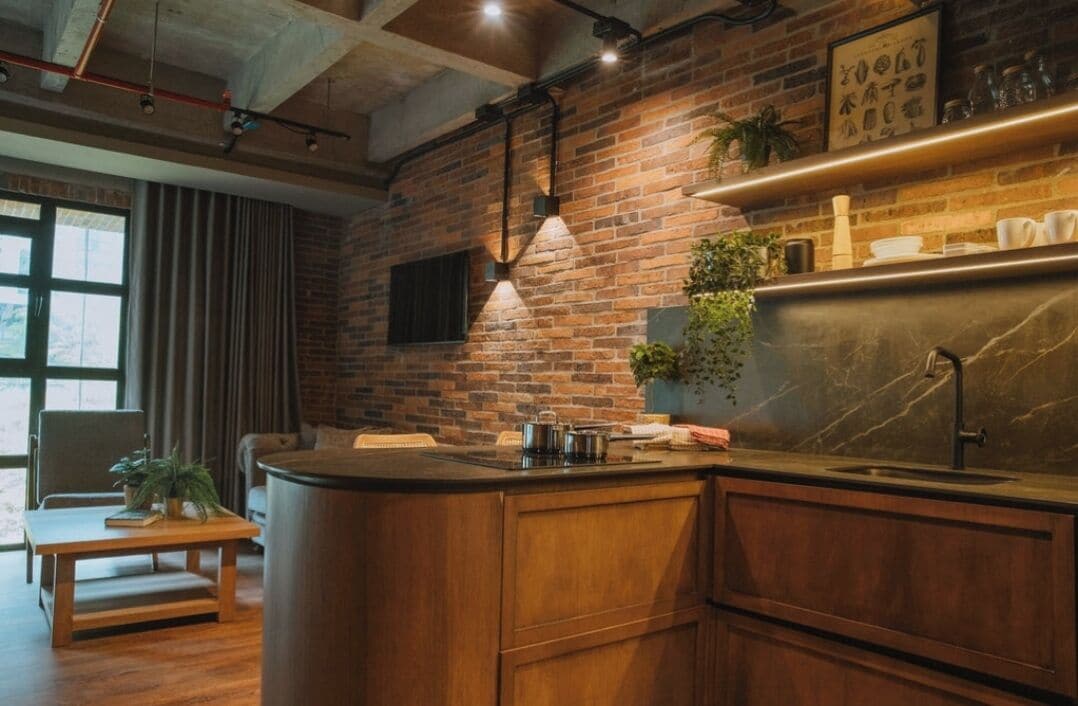 A kitchen with a brick wall, wooden cabinets, a marble countertop, and a hanging light fixture.