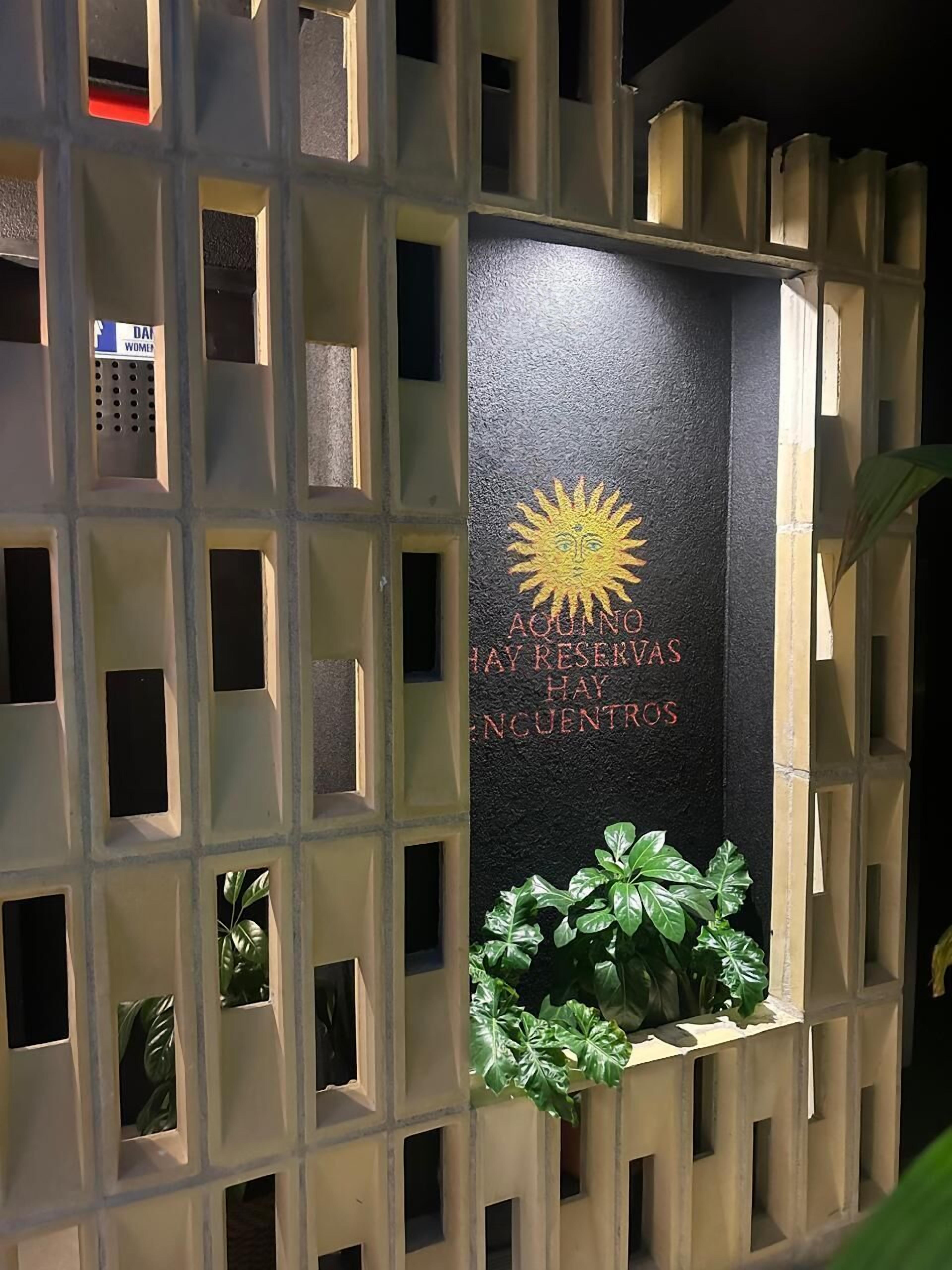 Una pared con un cartel que dice 'AQUINO HAY RESERVAS HAY ENCUENTROS' e ilustración de un sol.