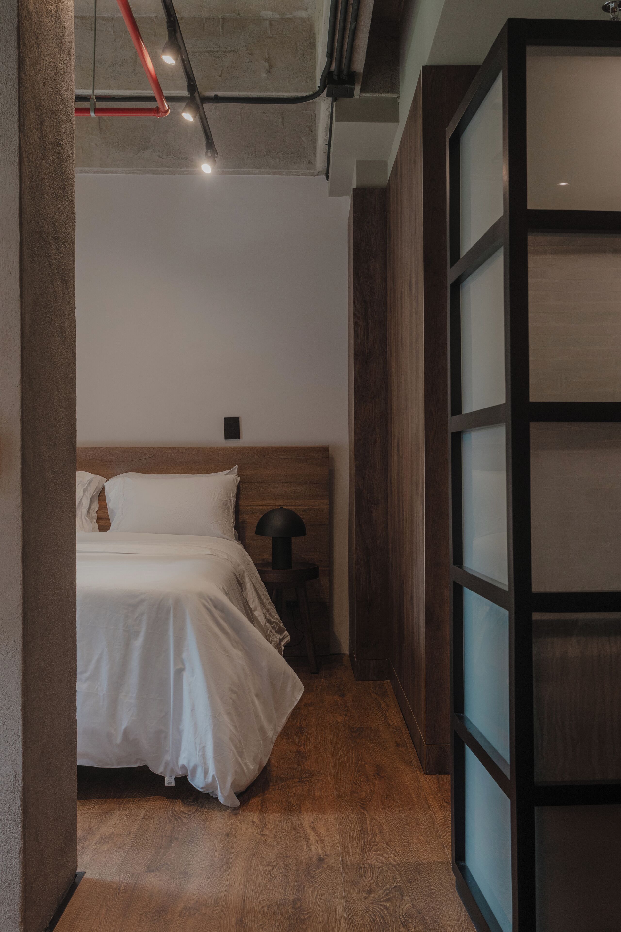 A bedroom with a wooden headboard, a bed with white bedding, a nightstand, and a large window with frosted glass panels.
