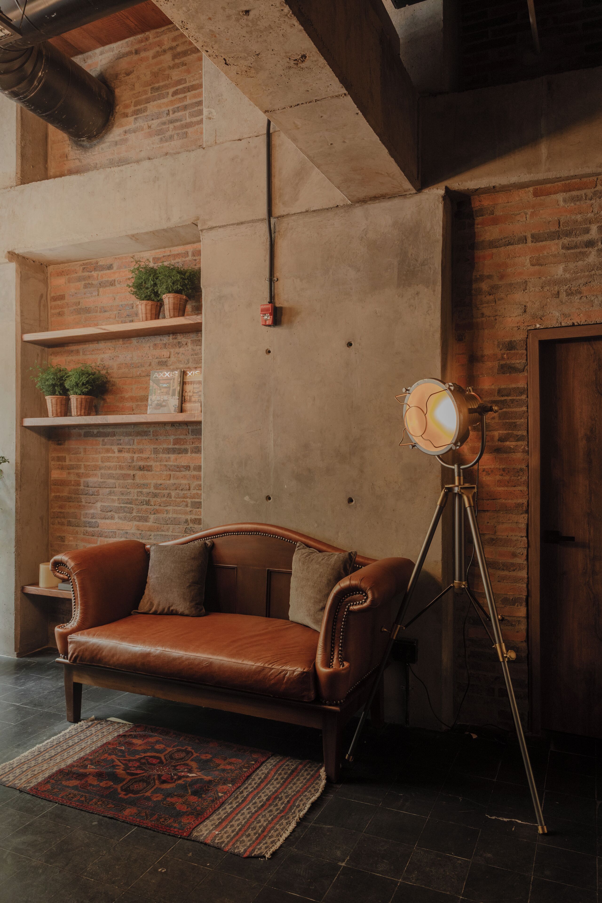 A room with a leather sofa, a floor lamp, and a brick wall with shelves.