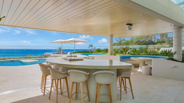 Un espace bar extérieur moderne, doté d’une piscine et offrant une vue sur l’océan.