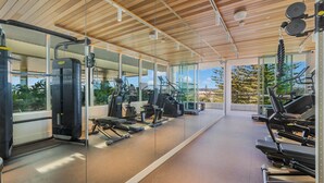 Un gimnasio moderno con máquinas de cardio, equipo de entrenamiento de pesas y amplias ventanas con vistas al exterior.