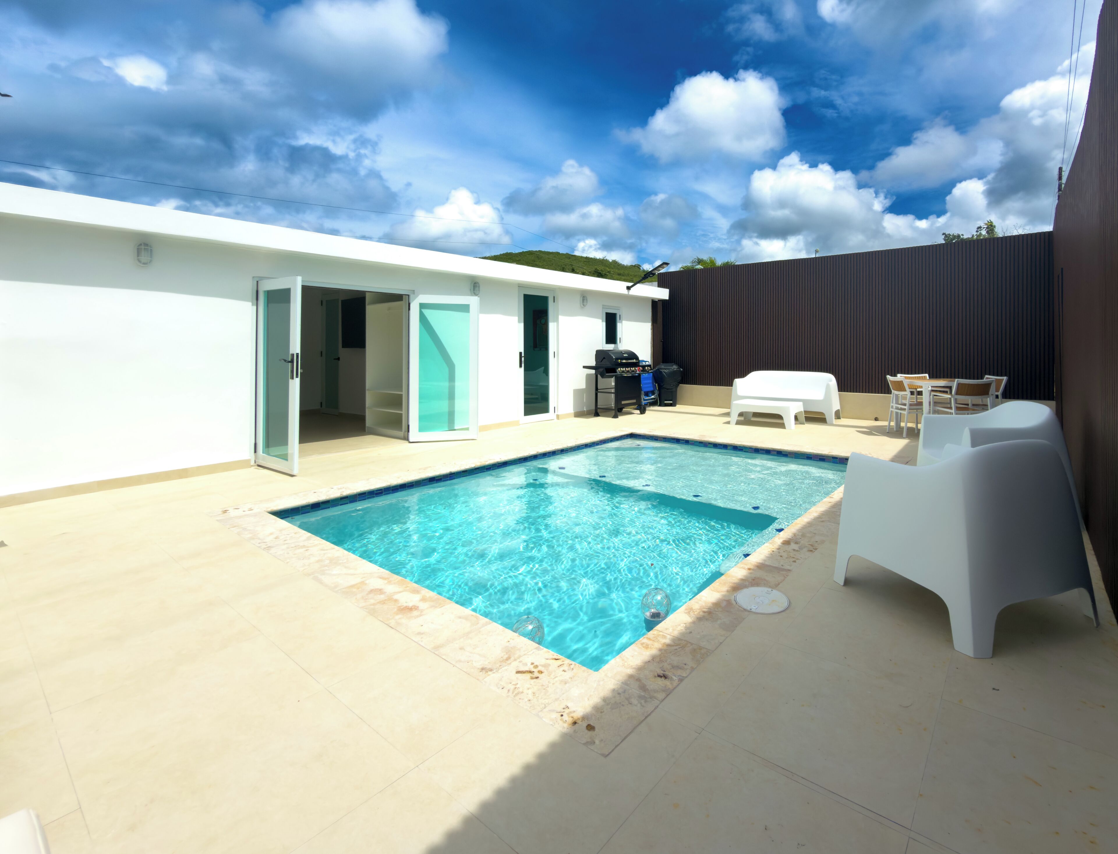 Ein Swimmingpool mit gefliestem Deck, einer Grillgelegenheit und Sitzmöglichkeiten im Freien.