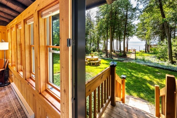 A wooden cabin with a deck and a view of a grassy area with a picnic table.