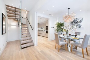 Un intérieur moderne avec un escalier en verre, un coin repas doté d’une table en verre et une cuisine en arrière-plan.