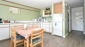 A compact kitchen with a dining table, chairs, a microwave, and a refrigerator.