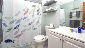 A bathroom with a shower curtain featuring fish patterns, a toilet, a sink with toiletries, and a mirror above the sink.