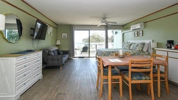 A room with a dining table, chairs, a sofa, a TV, and a ceiling fan.