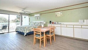 A room with a bed, a dining table with chairs, a kitchenette, and a balcony.
