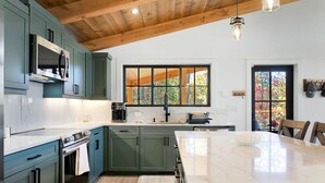 A modern kitchen with teal cabinets, a large island, and a wooden ceiling. - This is The Life - stunning mountain and lake view (Glenville)