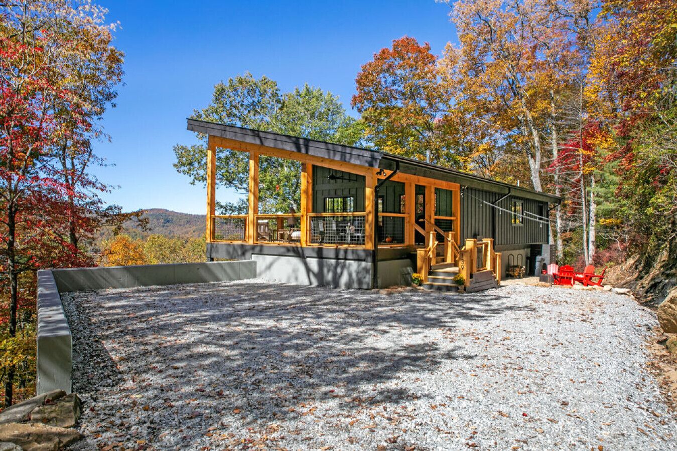 A modern cabin with a large deck, surrounded by autumn foliage.