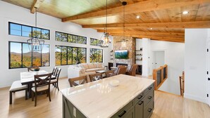 A spacious kitchen with a large island, wooden ceiling beams, and large windows offering a view of the outdoors. - This is The Life - stunning mountain and lake view (Glenville)