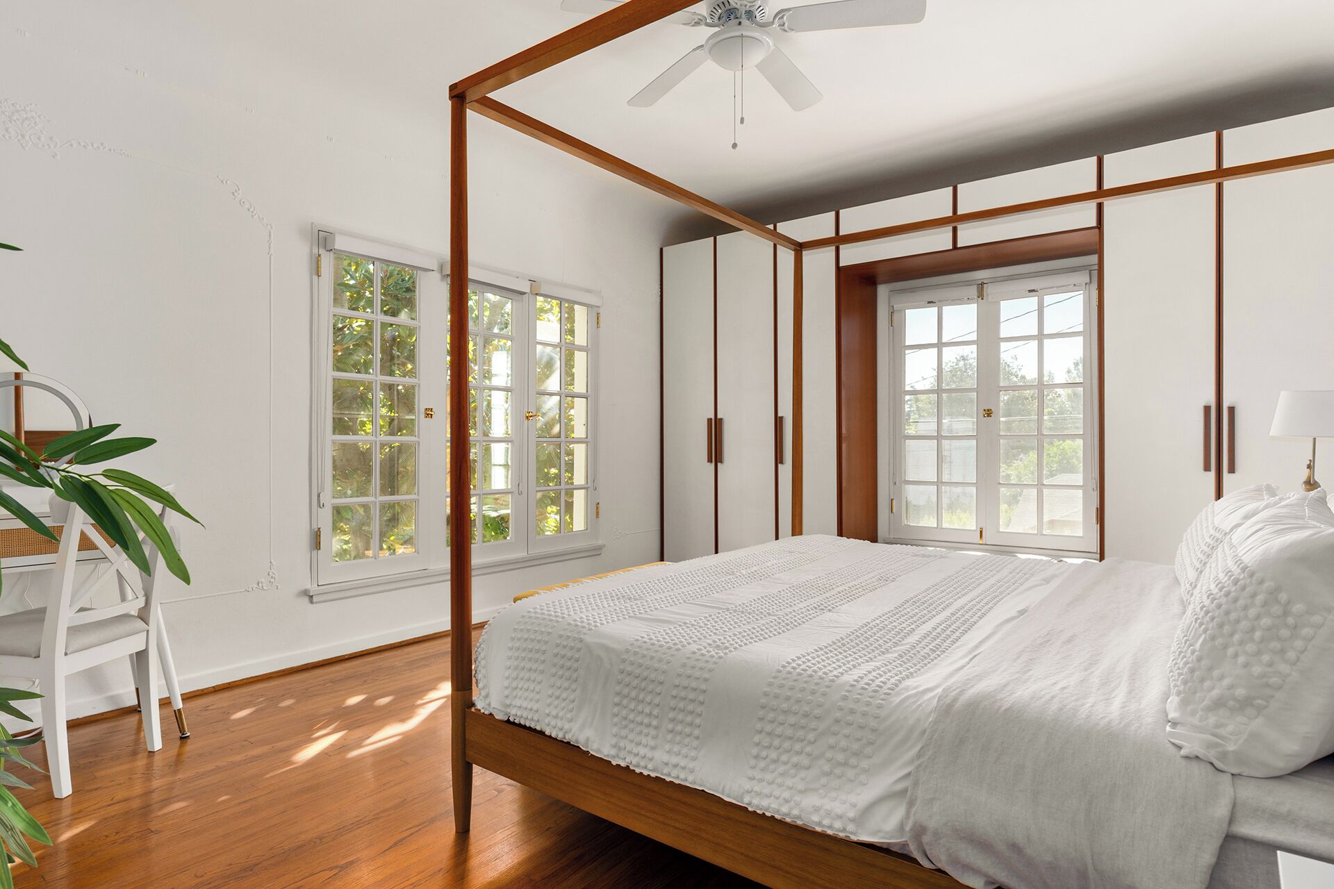 A bedroom with a wooden bed, white walls, and large windows.