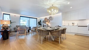 A modern living room with a dining area, featuring a chandelier, wicker furniture, and a large window. - Acqua Beach by Atlantic Holiday (Funchal)