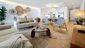 A modern living room with a sofa, coffee table, and chairs. There is a dining area with a table and chairs. The kitchen is visible in the background. - Acqua Beach by Atlantic Holiday (Funchal)