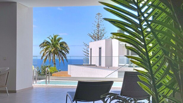 A balcony with a pool, two lounge chairs, and a view of the ocean and palm trees. - Acqua Beach by Atlantic Holiday (Funchal)