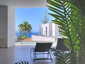 A balcony with a pool, two lounge chairs, and a view of the ocean and palm trees. - Acqua Beach by Atlantic Holiday (Funchal)