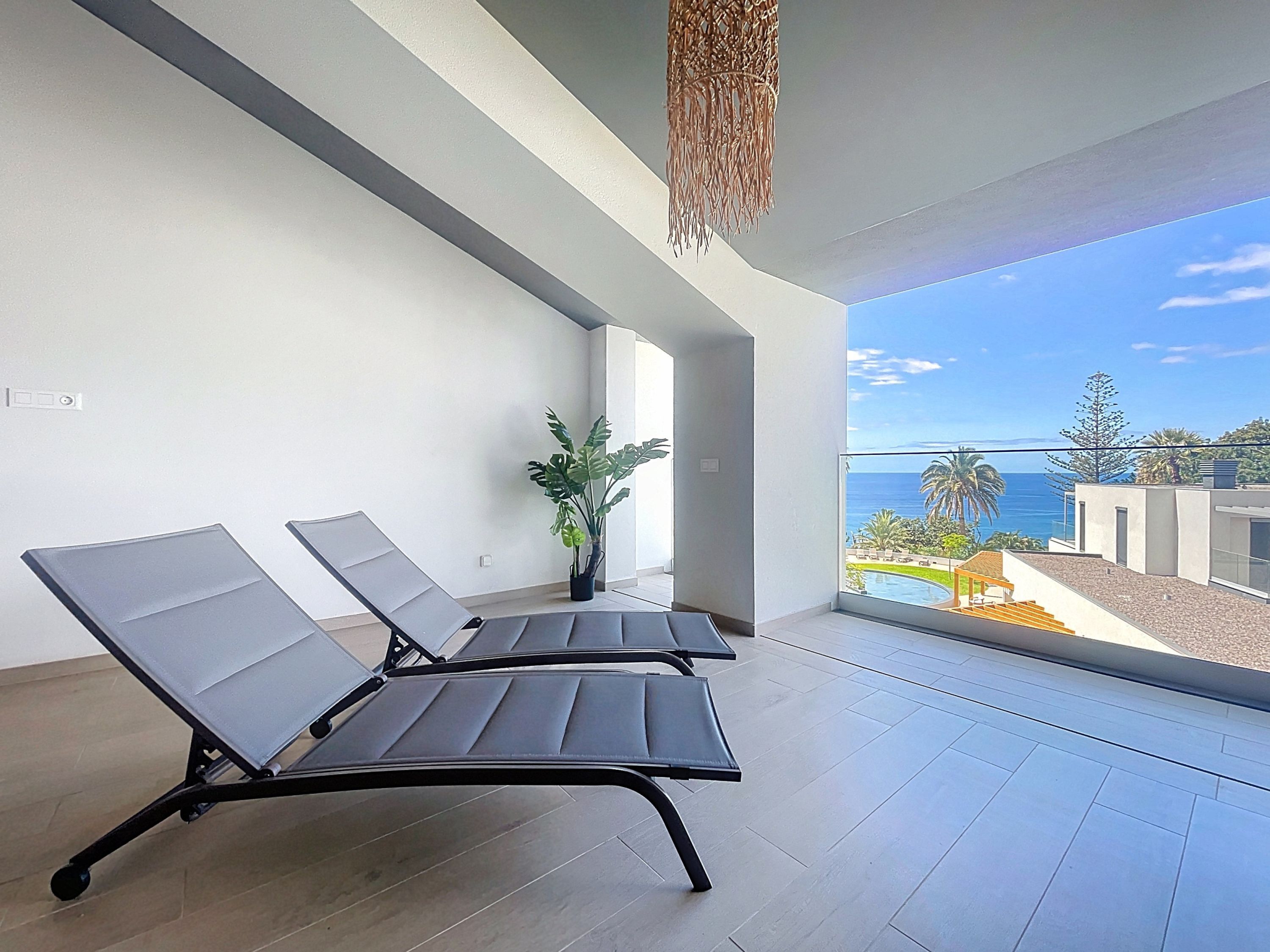 A balcony with two lounge chairs, a potted plant, and a view of the ocean.