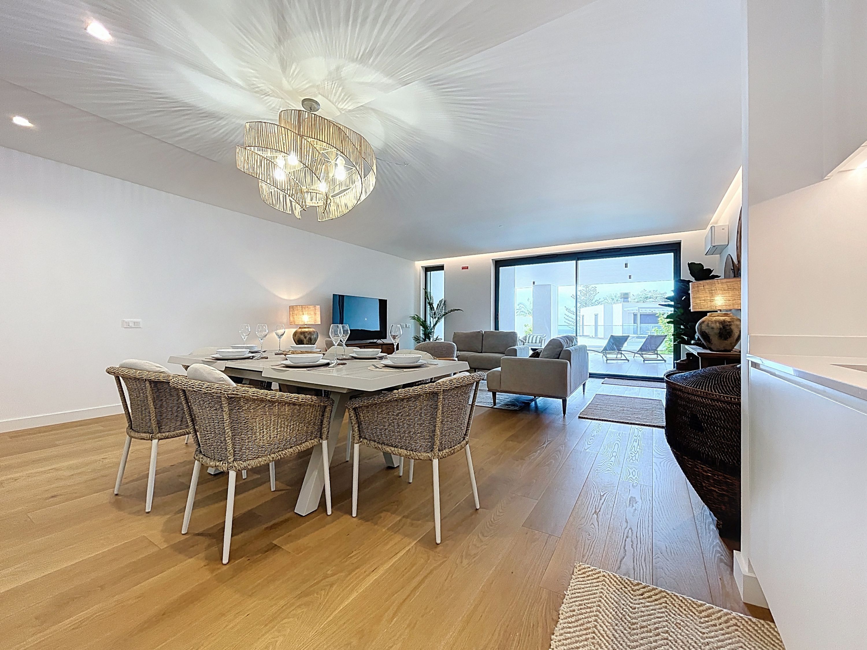 Un espace repas moderne agrémenté d’un lustre, de chaises en osier et d’un téléviseur à écran plat.