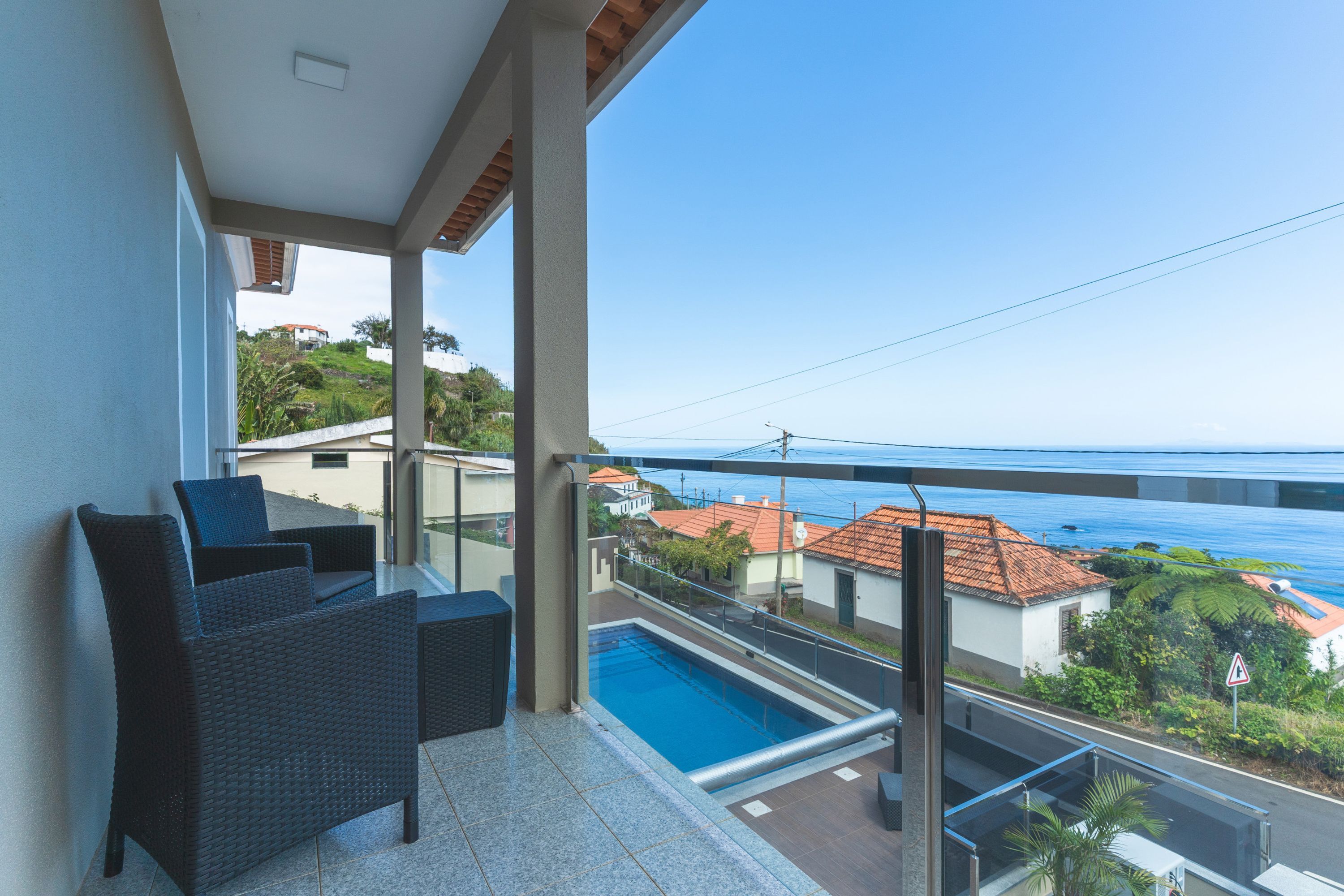 A balcony with a pool, outdoor furniture, and a view of the sea and buildings.