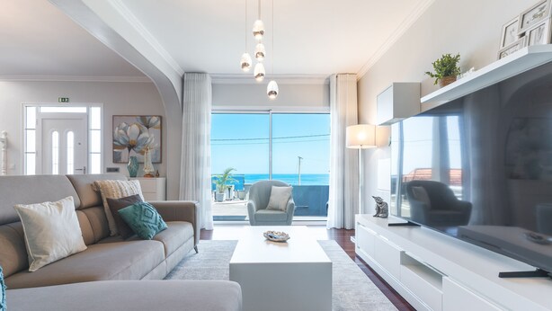 A modern living room with a sofa, coffee table, TV, and a balcony with a view. - Villa Alves by Atlantic Holiday (Santana)