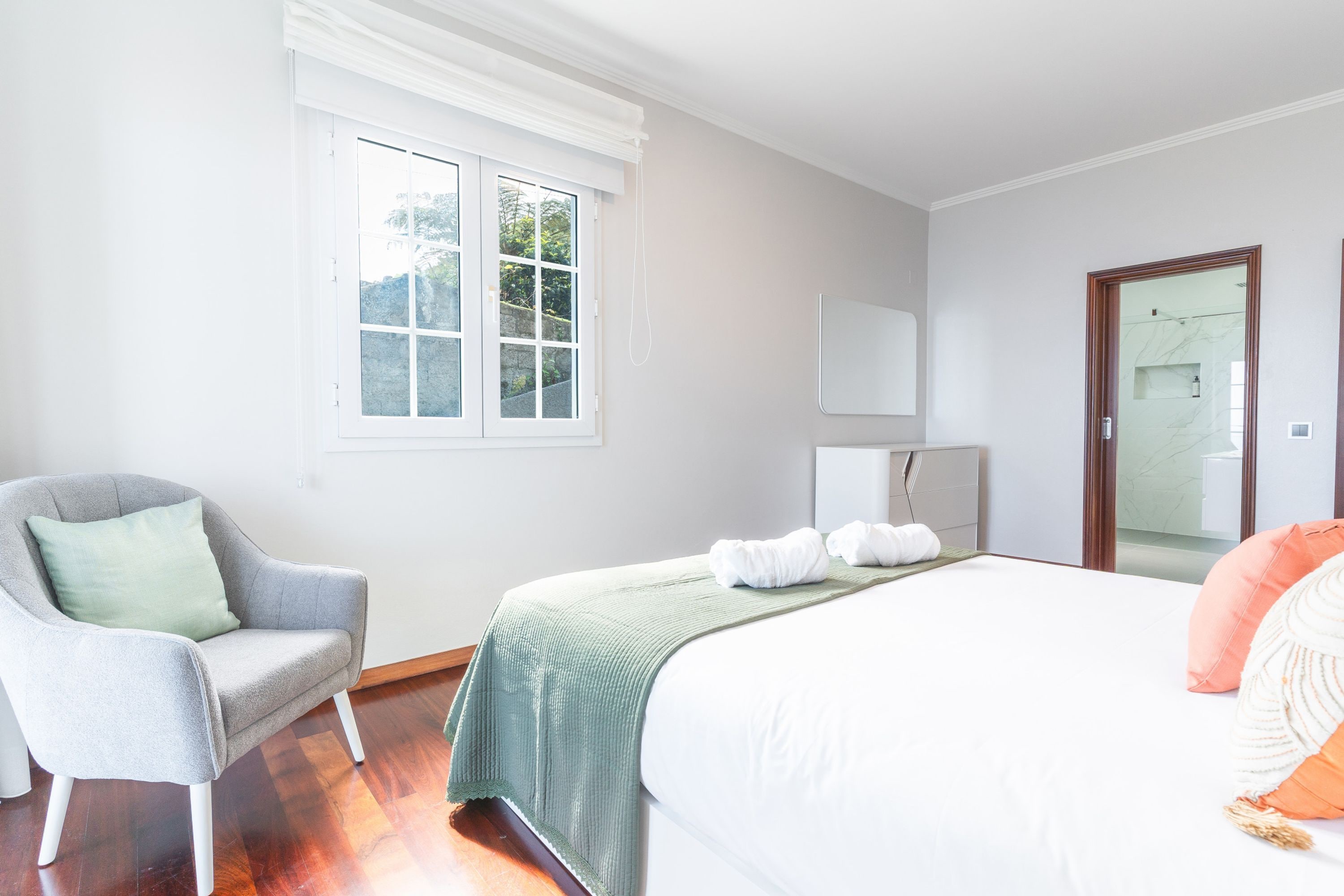 A bedroom with a bed, a chair, a window, and a mirror.