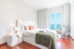 Una habitación de hotel moderna con una cama grande, una mesita de noche, una silla y vistas al océano por la ventana.
