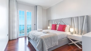 A modern bedroom with a large bed, a nightstand, and a view of the ocean through a sliding glass door. - Villa Alves by Atlantic Holiday (Santana)