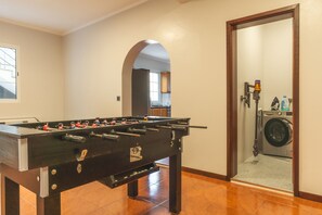 A room with a foosball table, a washing machine, and a door leading to a kitchen area. - Villa Alves by Atlantic Holiday (Santana)