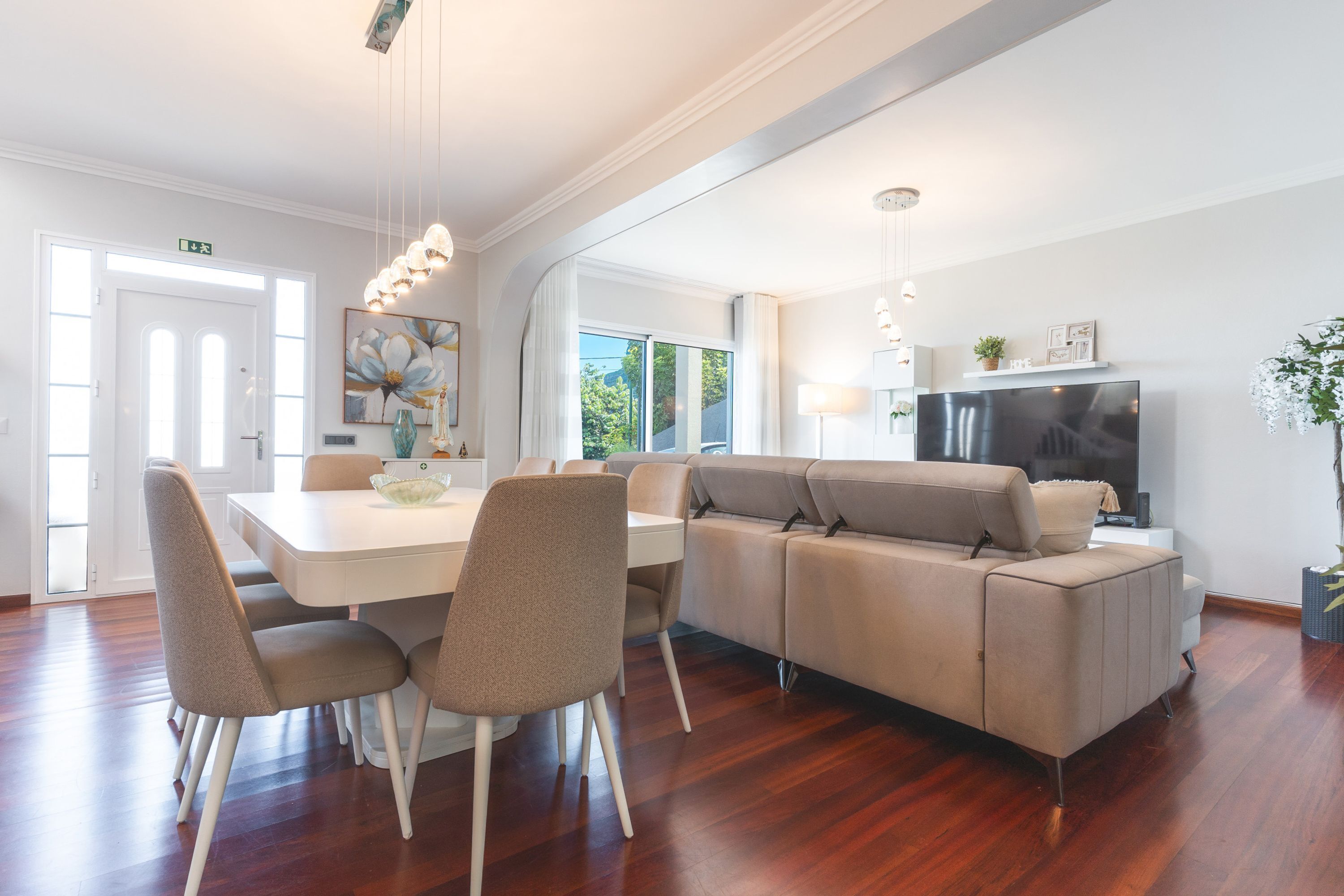 A modern living room with a white sofa, a dining table with chairs, and a flat-screen TV.