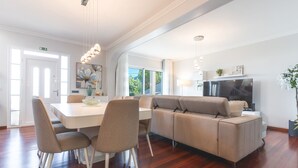 A modern living room with a white sofa, a dining table with chairs, and a flat-screen TV. - Villa Alves by Atlantic Holiday (Santana)