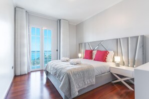 A modern bedroom with a large bed, a nightstand, and a view of the ocean through a sliding glass door. - Villa Alves by Atlantic Holiday (Santana)